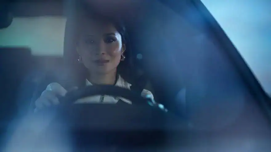 Woman confidently driving a car at night, focused expression, blue lighting.