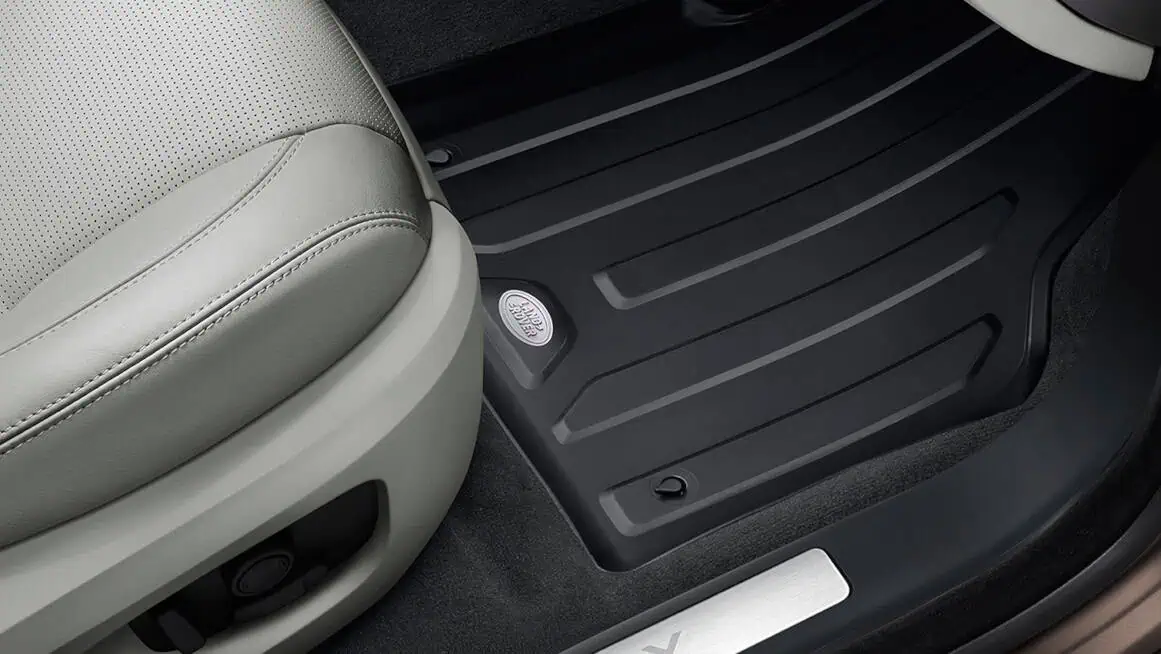 Modern Land Rover vehicle interior with premium floor mats and beige leather seat.