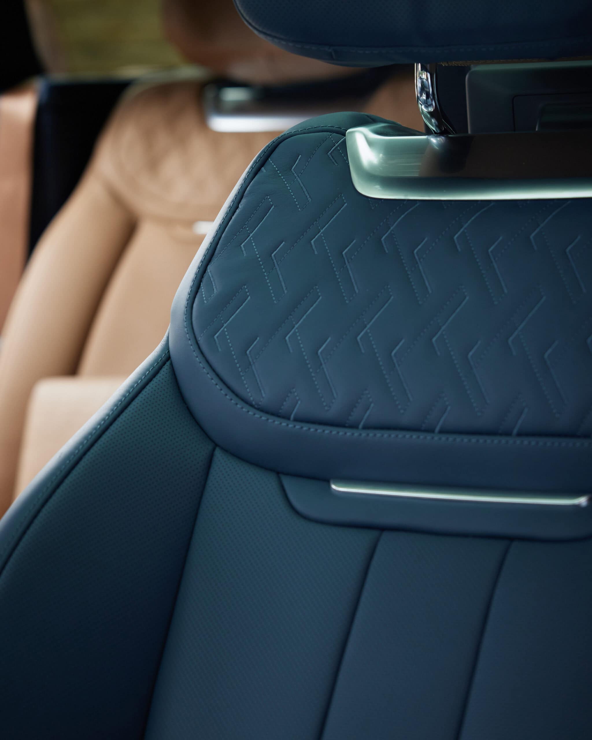 Close-up of a dark blue car seat with a detailed geometric pattern and metallic trim, with a tan seat visible in the background.