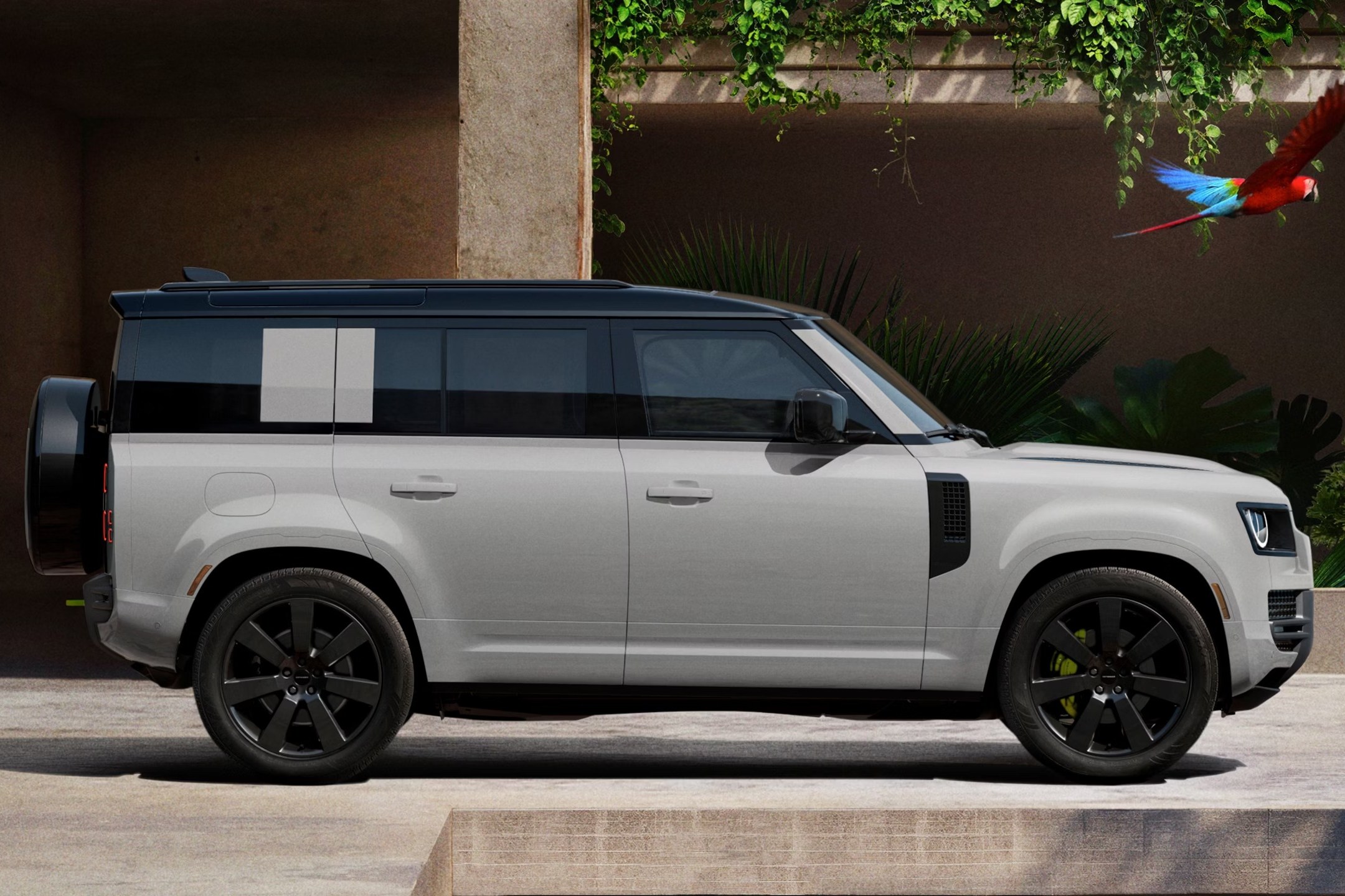 2027 Land Rover Defender side view parked by a stone wall with tropical plants