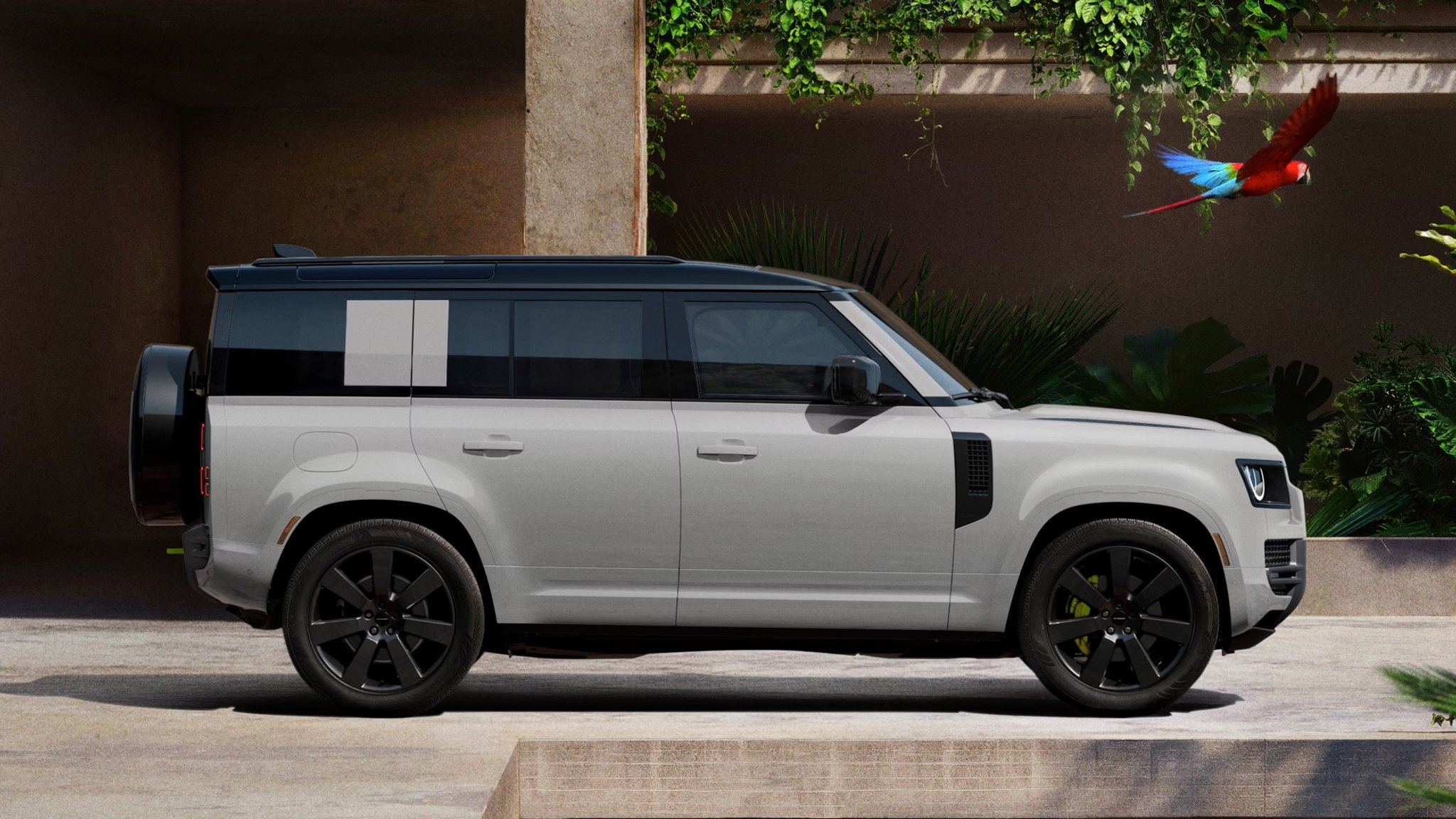 2027 Land Rover Defender side view parked near a tropical wall with a parrot
